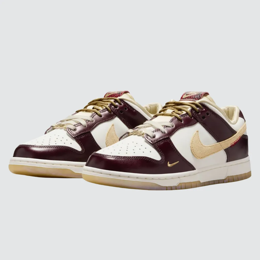 Tênis Nike Dunk Low Year of the Snake com cabedal em couro esbranquiçado, sobreposições borgonha, Swoosh em camurça bronzeada, detalhes em pele de cobra sintética na língua e solado translúcido, celebrando o Ano Novo Lunar com design simbólico e streetwear sofisticado.