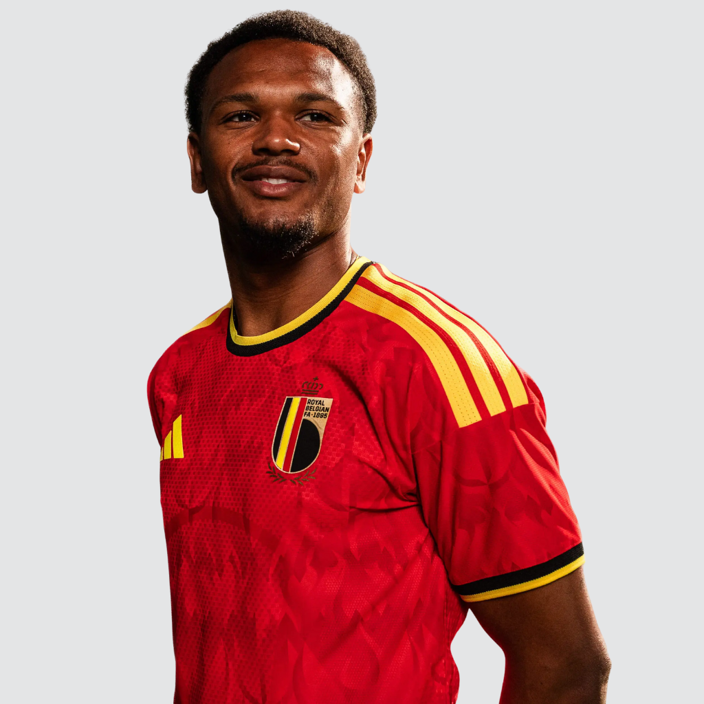 Camisa titular Bélgica 2026 exibida em ambiente esportivo, destacando o vermelho intenso e os grafismos de chamas e tridentes.