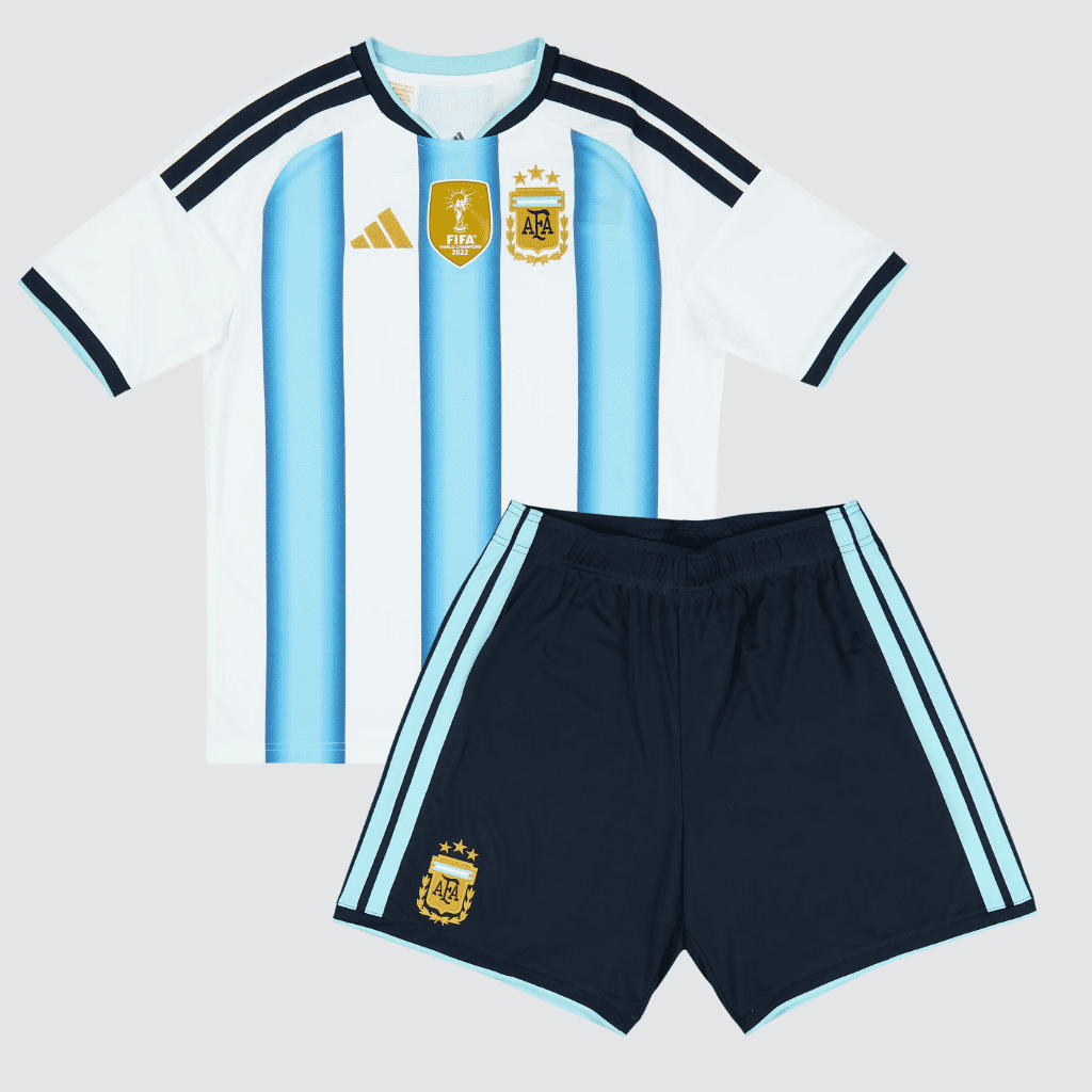 Conjunto infantil Argentina 2026 adidas branco e azul celeste com patch de tricampeão e calção azul-marinho.