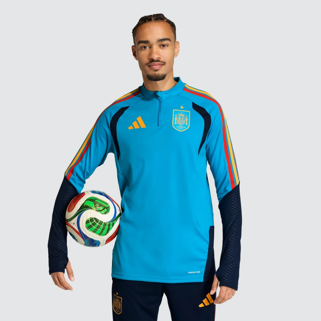 Atleta vestindo o conjunto de treino Espanha 2026 de frente, mostrando camisa azul com zíper e calça ajustada.