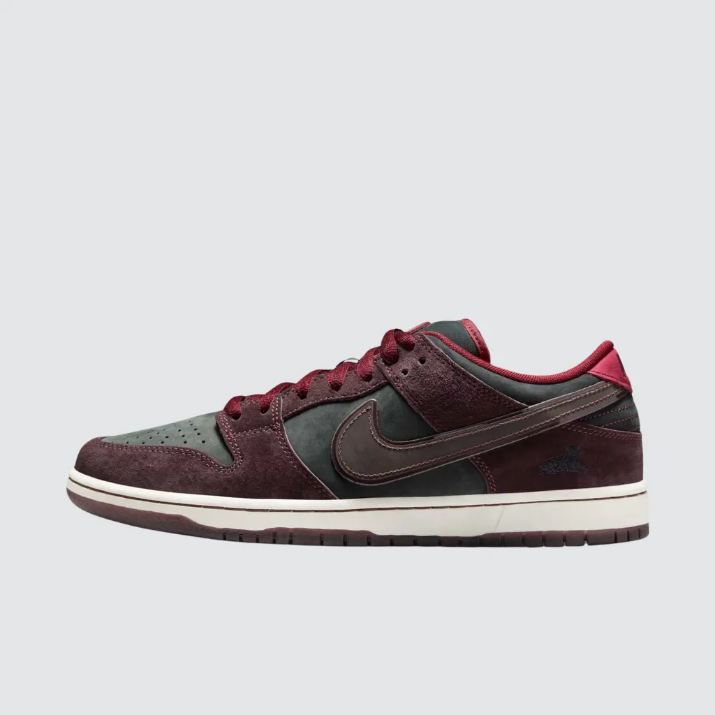 Tênis Nike RIOT Skateshop x Dunk Low SB Mahogany Dark Beetroot com cabedal em nobuck e camurça premium, tons vinho e verde escuro, Swoosh bordô com contorno brilhante, palmilha de cortiça artística e solado translúcido, representando uma colaboração entre cultura skate e herança urbana francesa.